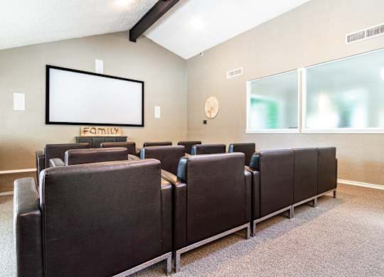 a small conference room with brown leather chairs and a white screen on the wall