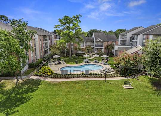 A swimming pool surrounded by grass and trees in a residential area.
