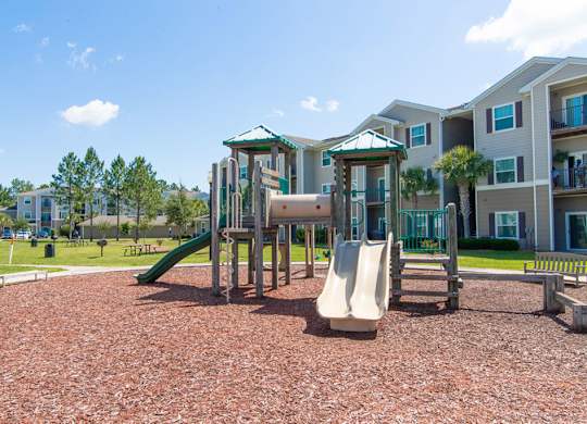 A playground with a green slide and a white slide in front of apartment buildings.