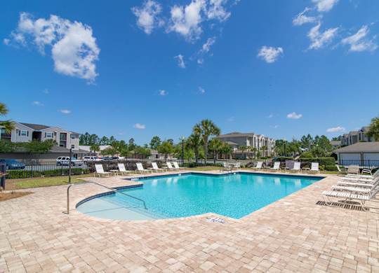 A large swimming pool surrounded by a brick patio and lounge chairs.