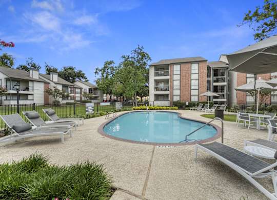 A swimming pool surrounded by lounge chairs and umbrellas in a residential area.