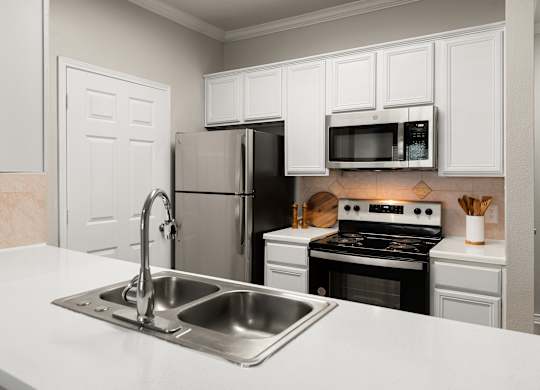 Kitchen pass-through with double sink, white cabinetry, and stainless steel appliances.