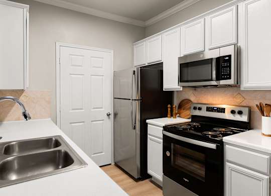 Kitchen with white cabinetry, stainless steel refrigerator, microwave, range, and double sink.