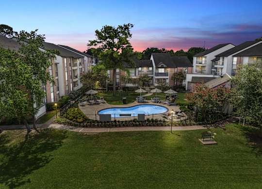 A swimming pool surrounded by grass and trees in a residential area.