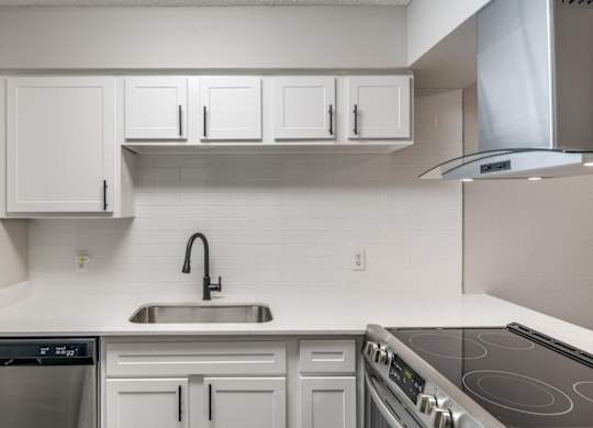 White kitchen counter with undermount sink, white tile backsplash, and electric range.
