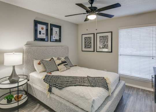 Serene bedroom with upholstered bed, ceiling fan, and large window blinds.