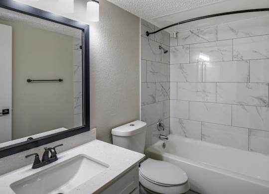Bathroom with tub-and-shower combo, marble-look tile surround, and single-sink vanity.