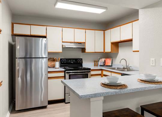 Classic kitchen with white cabinetry, breakfast bar, and stainless steel refrigerator at Heritage at Valley Ranch, Irving, TX.