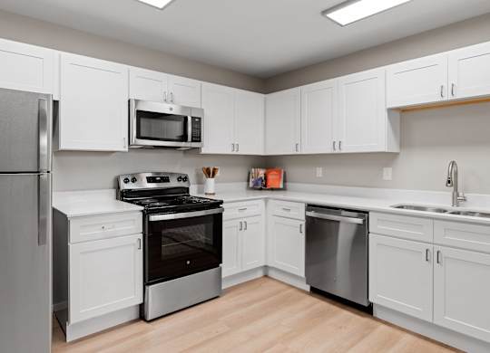 Updated apartment kitchen with wraparound counters, white cabinetry, and stainless steel dishwasher and range.