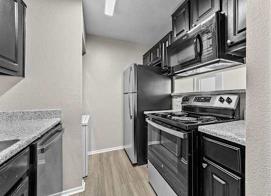 Galley-style kitchen with dark cabinetry, stainless steel appliances, and durable wood-style flooring.