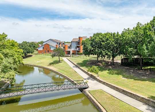 Scenic pond with footbridge, walking path, and open green space beside the community.