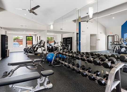 Spacious fitness center with free weights, cardio machines, mirrored wall, and vaulted ceiling.