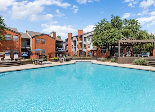 Sparkling swimming pool with pergola lounge area and surrounding brick apartment buildings.