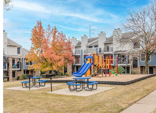 A playground with a blue slide and picnic tables in front of a row of houses.