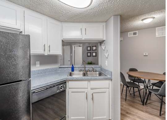 A kitchen with a black refrigerator, white cabinets, and a wooden table.