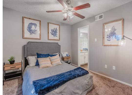 A bedroom with a bed, a ceiling fan, and three wall art pieces.