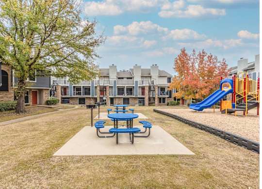 A playground with a blue slide and picnic table in the foreground.
