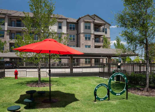 a park with a red umbrella in front of an apartment building