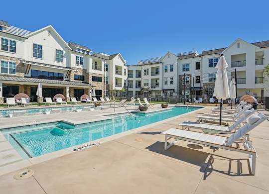 a swimming pool with lounge chairs and umbrellas in front of an apartment building