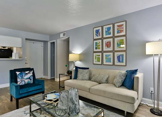 A living room with a blue chair, a beige couch, and a glass coffee table.