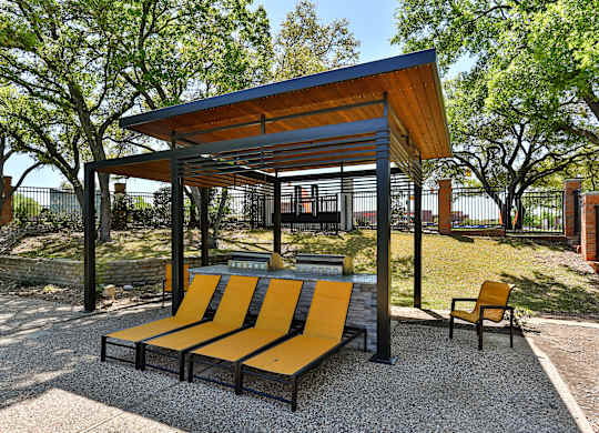 A park bench with a yellow and black design is situated under a wooden and metal shelter.
