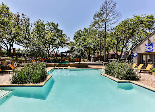 A large outdoor swimming pool surrounded by trees and plants.