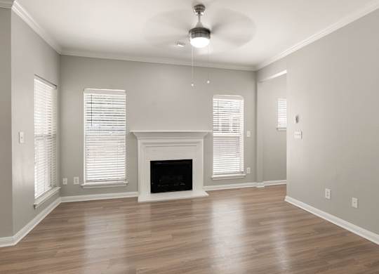 Open living room with wood-style flooring, white fireplace mantel, ceiling fan, and tall windows.