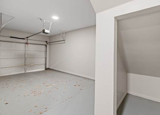 Attached garage interior with overhead door, painted concrete floor, and under-stair storage nook.