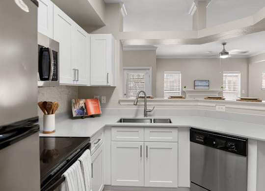 Open kitchen with breakfast bar, double-basin sink, dishwasher, and view into living area.