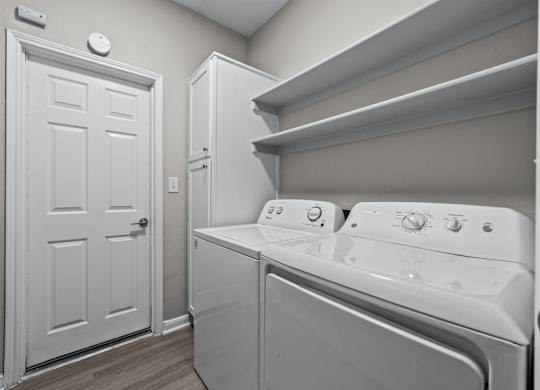 Laundry room with full-size washer and dryer, upper shelving, and storage cabinet.