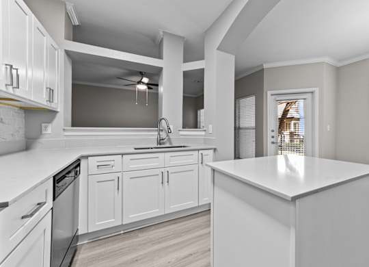 White kitchen island with surrounding cabinetry, breakfast bar, and nearby patio door.