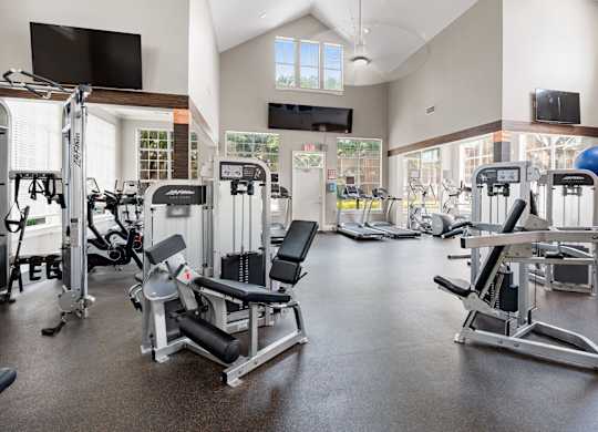Spacious fitness center with strength machines, cardio equipment, vaulted ceilings, and large windows.