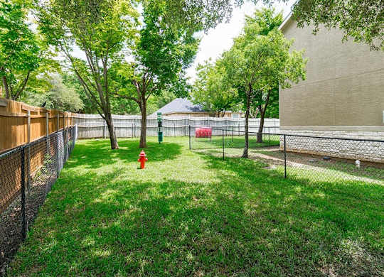 A backyard with a fence, trees, and a fire hydrant.