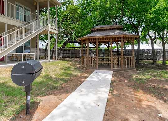 A gazebo is located in a yard with a mailbox in front of it.