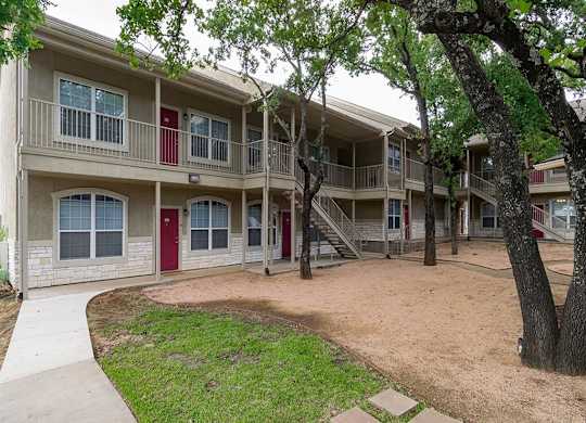 Apartment complex with a red door and a tree in front.