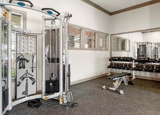 Strength training room with cable machine, dumbbell rack, bench, and full wall mirrors.