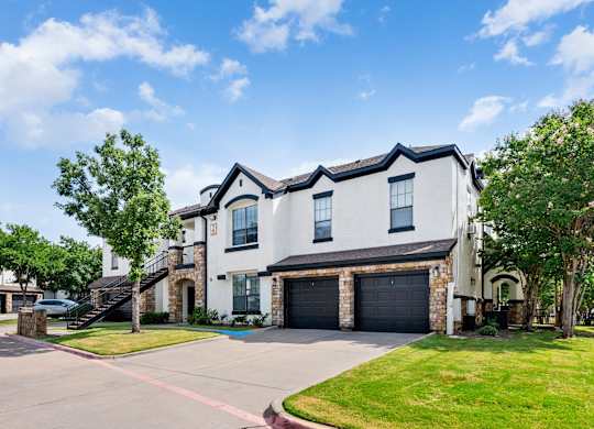 Apartment building exterior with attached garages, exterior staircase, and manicured lawn.