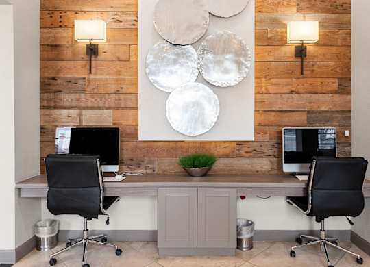 Business center with two desktop computers, leather chairs, and wood accent wall.