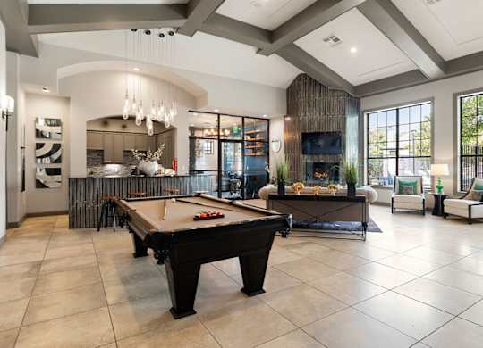 Clubhouse lounge with billiards table, seating area, large windows, and open kitchen bar.