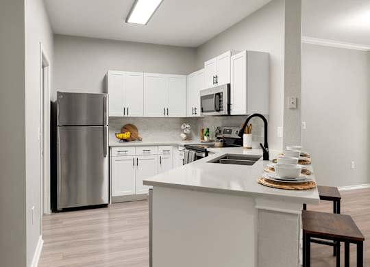 Kitchen with white shaker cabinets, breakfast bar, stainless steel appliances, and open layout.