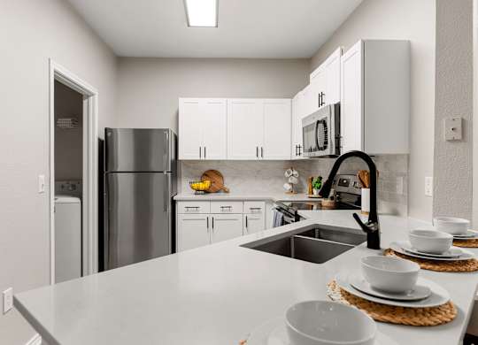 Modern kitchen with white cabinetry, breakfast bar, laundry closet, and stainless steel appliances.