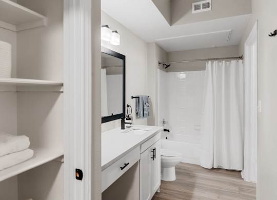 Bathroom with single vanity, large framed mirror, open shelving, and tub-shower combination.