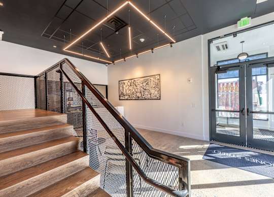 A staircase with a metal railing leads to a brightly lit room with a large painting on the wall.