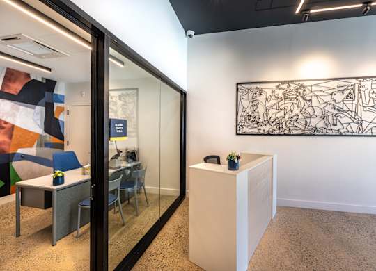 A room with a glass wall, a white reception desk, and a large black and white drawing on the wall.