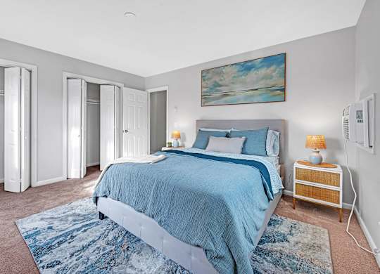 A bedroom with a blue bedspread and a painting on the wall.