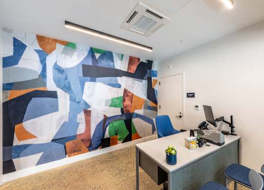 A room with a desk and a large abstract painting on the wall.