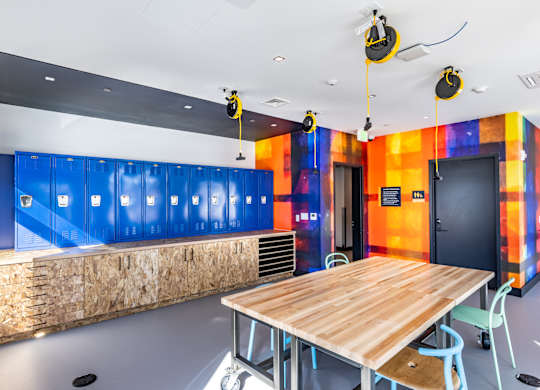 A room with a wooden table and chairs, a ceiling fan, and a wall with a blue and orange design.