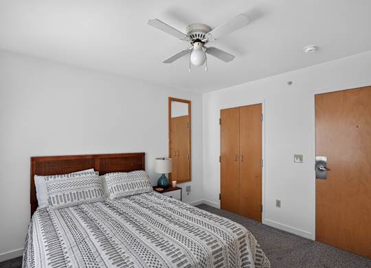 A bedroom with a bed, nightstand, and a ceiling fan.