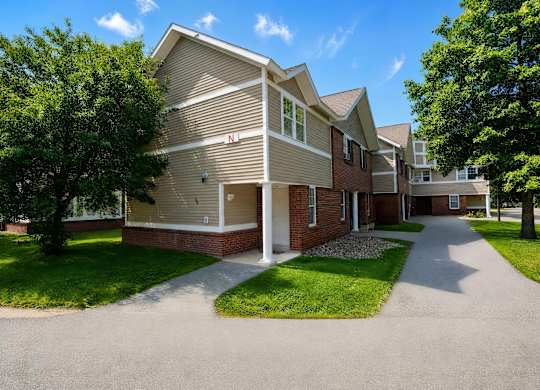 A residential building with a driveway and trees in front.