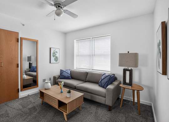 A living room with a grey couch, a wooden coffee table, and a ceiling fan.